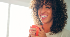 A smiling woman enjoying a cup of coffee, representing improved mental and physical well-being through dietary adjustments.