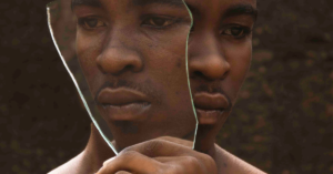 A man holding a broken mirror, illustrating the fragmented perception and self-reflection often associated with late-diagnosed neurodiversity.