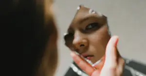 A woman looking into a broken piece of a mirror, symbolizing self-doubt, confusion, and the fractured reality caused by gaslighting.