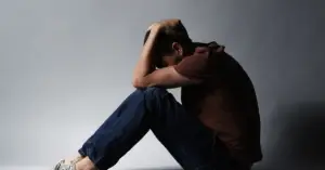 A man sitting alone, holding his head in his hands, symbolizing the isolation and emotional overwhelm often faced by neurodivergent individuals in toxic relationships.