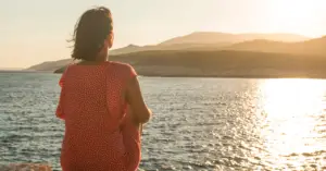 A woman sitting by the water, her back to the camera, symbolizing quiet reflection and the journey toward healing and self-discovery.