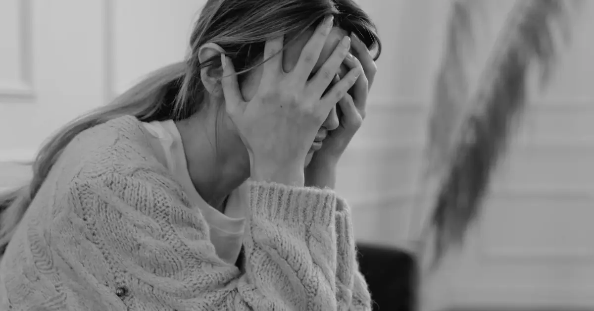 Black and white image of a woman sitting with her face in her hands, implying stress and workplace fatigue